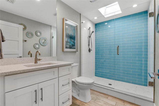 bathroom featuring a skylight, a stall shower, wood finished floors, vanity, and toilet