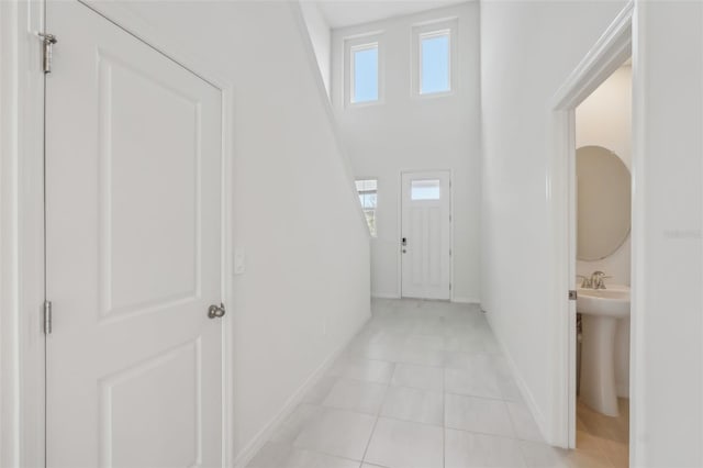 hallway with a high ceiling, light tile patterned floors, and baseboards