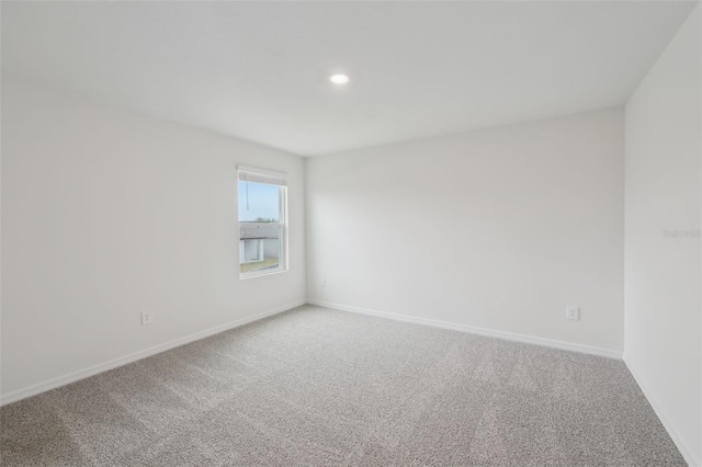 spare room featuring recessed lighting, light colored carpet, and baseboards