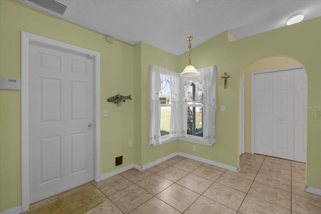 unfurnished dining area with light tile patterned flooring, lofted ceiling, and a textured ceiling