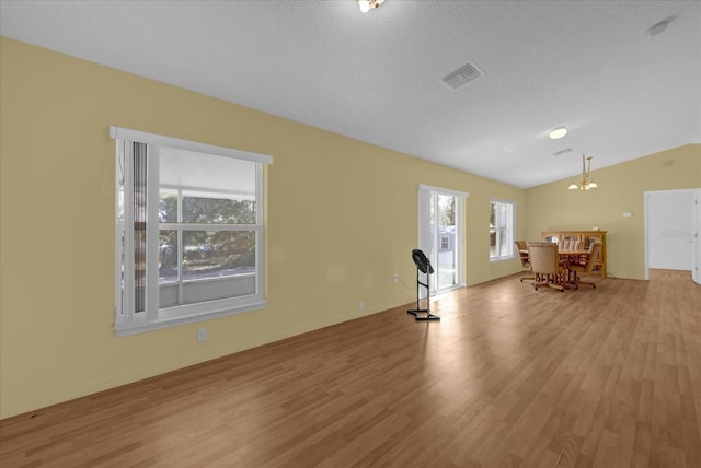 workout area featuring vaulted ceiling, a chandelier, a textured ceiling, and light wood-type flooring