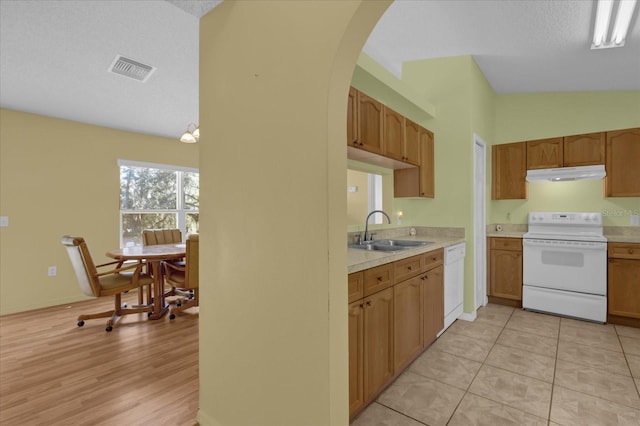 kitchen with sink, white appliances, a textured ceiling, light tile patterned flooring, and vaulted ceiling