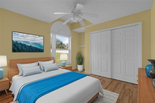 bedroom with light hardwood / wood-style flooring, a textured ceiling, ceiling fan, and a closet