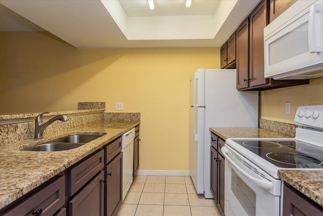 kitchen with light tile patterned flooring, sink, light stone counters, a tray ceiling, and white appliances