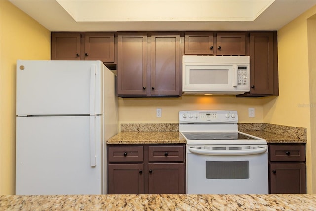 kitchen featuring dark brown cabinetry, light stone countertops, and white appliances