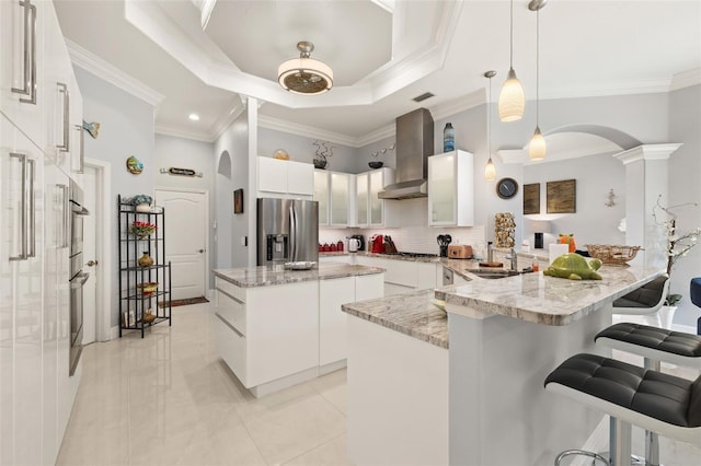 kitchen featuring stainless steel appliances, a center island, white cabinets, decorative light fixtures, and wall chimney exhaust hood