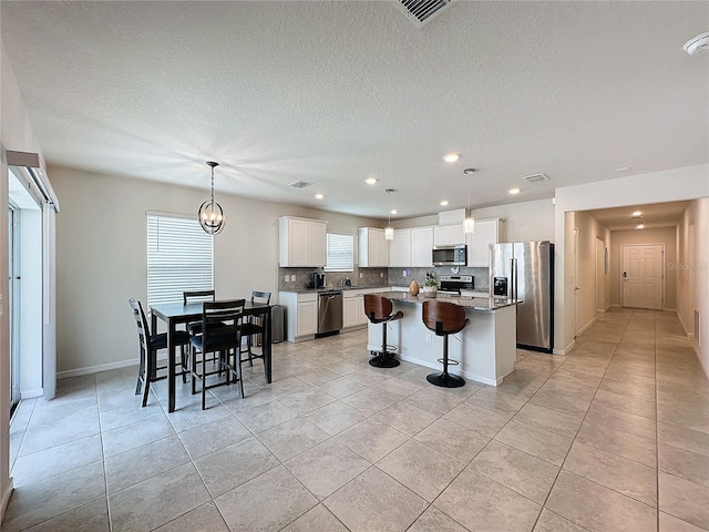 kitchen with light tile patterned floors, white cabinetry, hanging light fixtures, stainless steel appliances, and a center island