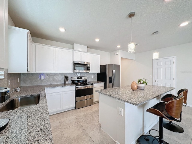 kitchen with pendant lighting, sink, appliances with stainless steel finishes, white cabinetry, and a kitchen island