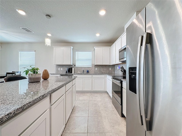 kitchen with appliances with stainless steel finishes, backsplash, light stone countertops, white cabinets, and decorative light fixtures