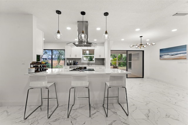 kitchen featuring white cabinetry, tasteful backsplash, kitchen peninsula, pendant lighting, and island exhaust hood