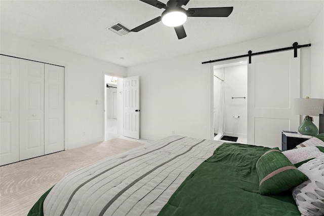 carpeted bedroom featuring ceiling fan, a barn door, a textured ceiling, ensuite bath, and a closet