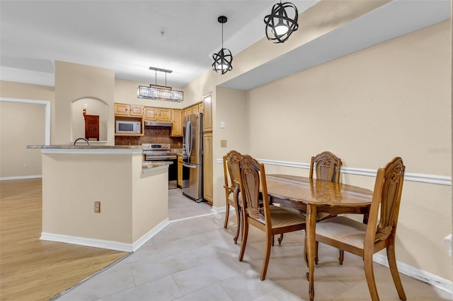 kitchen with light tile patterned floors, light brown cabinets, pendant lighting, stainless steel appliances, and backsplash