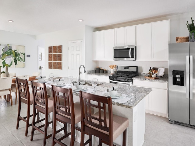 kitchen featuring sink, a kitchen breakfast bar, an island with sink, stainless steel appliances, and light stone countertops