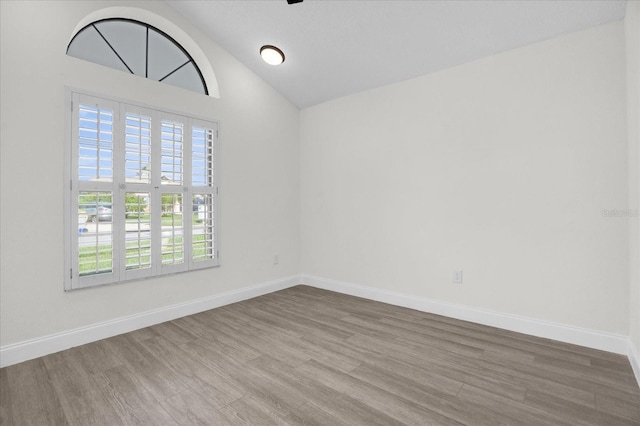 empty room with hardwood / wood-style floors and vaulted ceiling