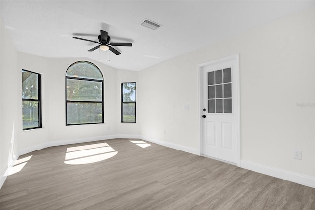 empty room with ceiling fan, lofted ceiling, a healthy amount of sunlight, and light hardwood / wood-style floors