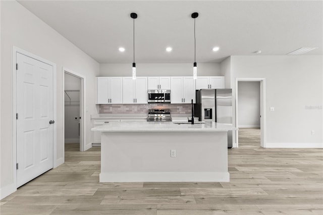 kitchen featuring an island with sink, appliances with stainless steel finishes, pendant lighting, and white cabinets