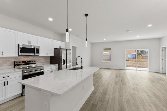 kitchen with sink, a kitchen island with sink, stainless steel appliances, light stone counters, and decorative light fixtures