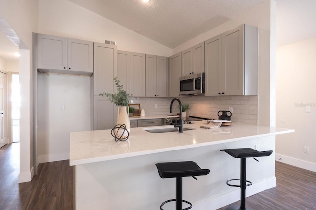 kitchen featuring sink, tasteful backsplash, vaulted ceiling, dark hardwood / wood-style flooring, and kitchen peninsula