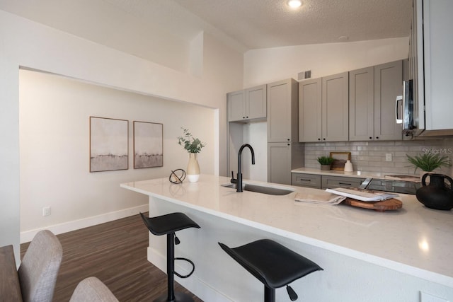 kitchen with sink, gray cabinets, dark hardwood / wood-style floors, tasteful backsplash, and vaulted ceiling