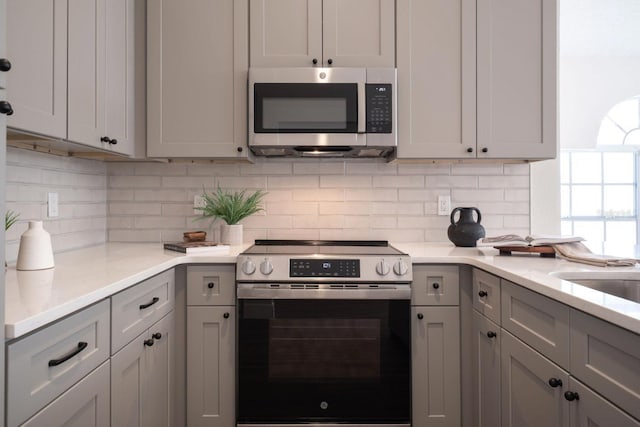 kitchen featuring tasteful backsplash, stainless steel appliances, light stone counters, and gray cabinetry