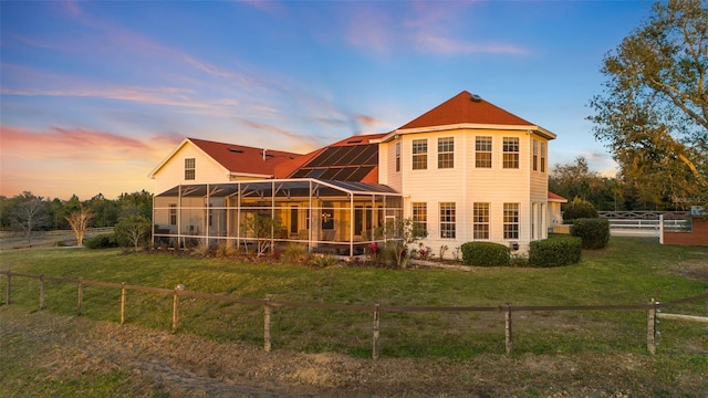 back house at dusk with a lanai and a lawn