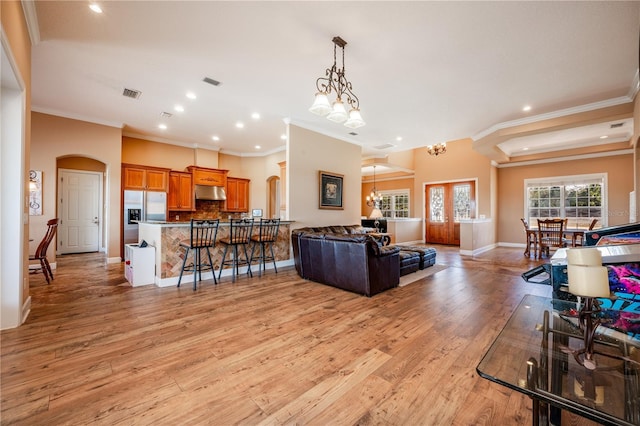 living room with an inviting chandelier, crown molding, light hardwood / wood-style flooring, and french doors