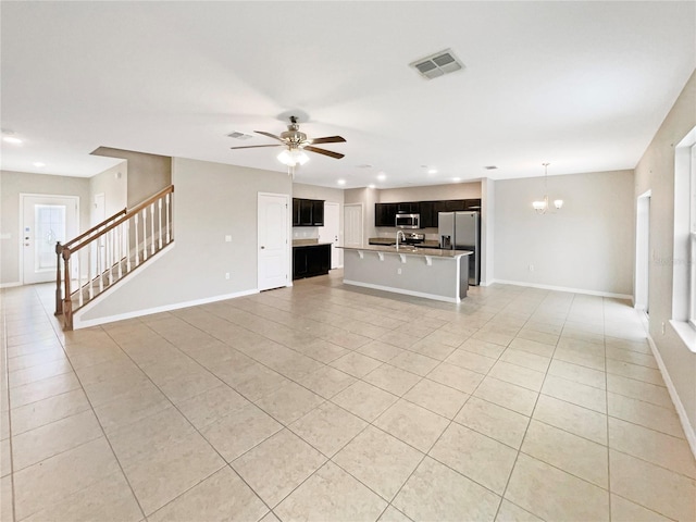 unfurnished living room with light tile patterned flooring, sink, ceiling fan with notable chandelier, and a healthy amount of sunlight