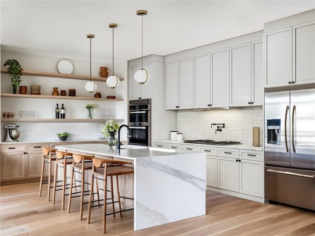 kitchen with pendant lighting, white cabinetry, a kitchen island with sink, light stone counters, and stainless steel appliances