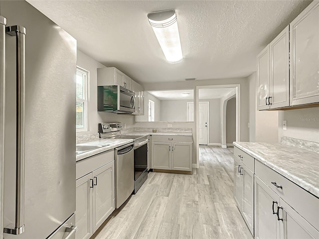 kitchen featuring appliances with stainless steel finishes, sink, a textured ceiling, and light hardwood / wood-style floors