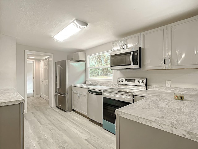 kitchen featuring gray cabinets, sink, light hardwood / wood-style floors, stainless steel appliances, and a textured ceiling