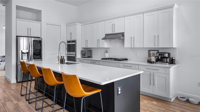 kitchen featuring white cabinetry, tasteful backsplash, appliances with stainless steel finishes, a kitchen breakfast bar, and a kitchen island with sink