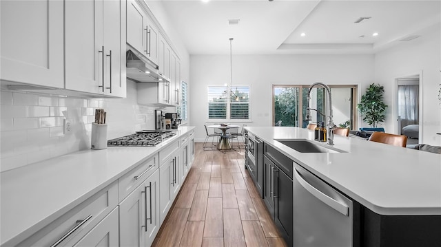 kitchen with appliances with stainless steel finishes, white cabinetry, an island with sink, sink, and hanging light fixtures