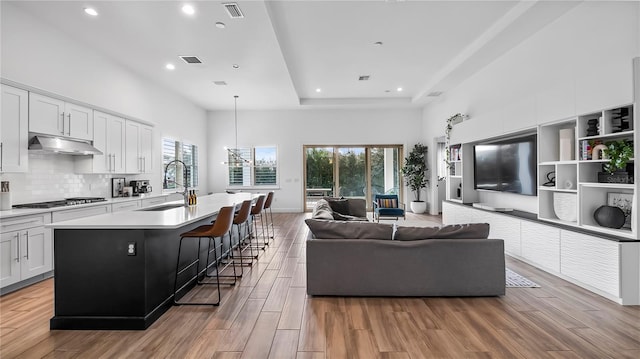 living room with a raised ceiling, a high ceiling, sink, and a notable chandelier