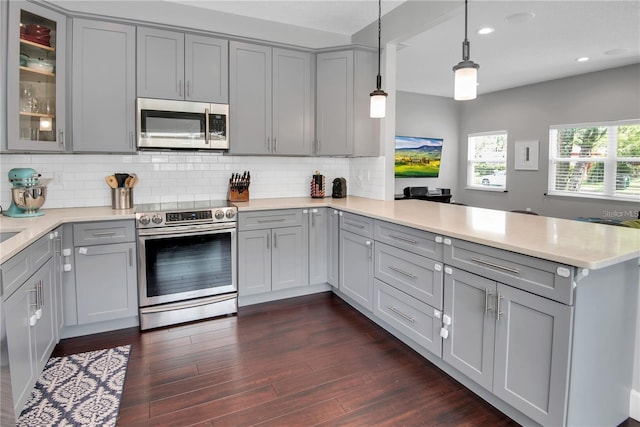 kitchen featuring gray cabinetry, hanging light fixtures, appliances with stainless steel finishes, kitchen peninsula, and decorative backsplash