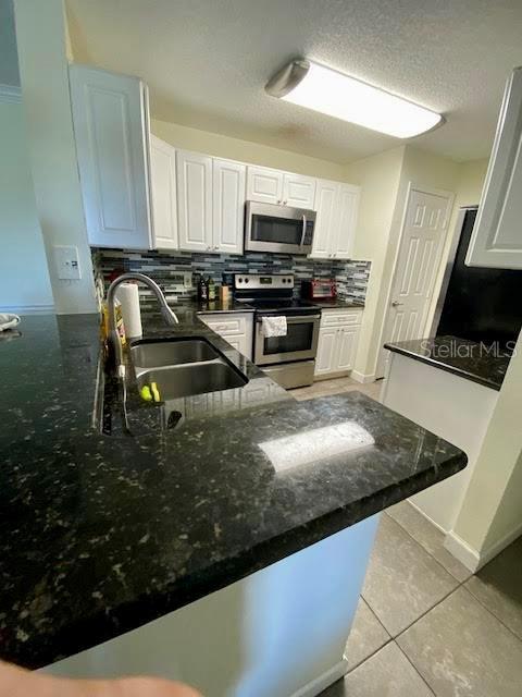 kitchen with sink, white cabinets, light tile patterned floors, kitchen peninsula, and stainless steel appliances