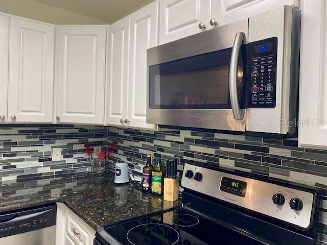 kitchen with white cabinetry, tasteful backsplash, stainless steel appliances, and dark stone countertops