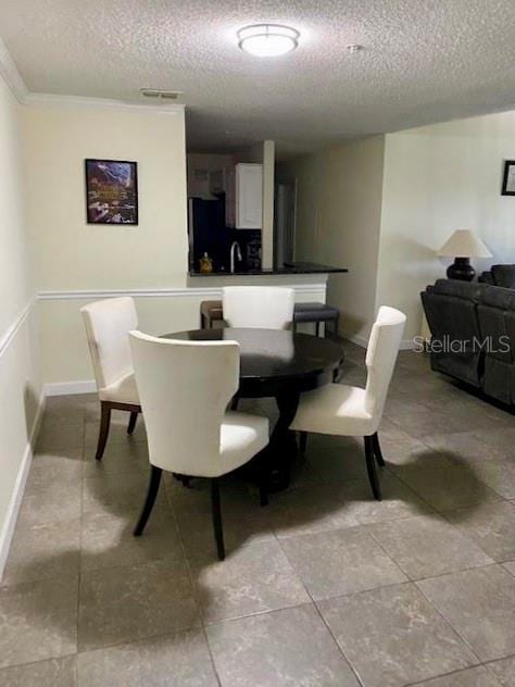 tiled dining area with sink, crown molding, and a textured ceiling