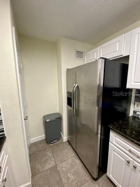 kitchen with stainless steel refrigerator with ice dispenser, dark stone countertops, light tile patterned floors, and white cabinets