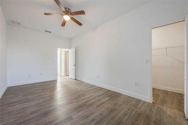 unfurnished bedroom featuring a spacious closet, dark wood-type flooring, ceiling fan, and a closet