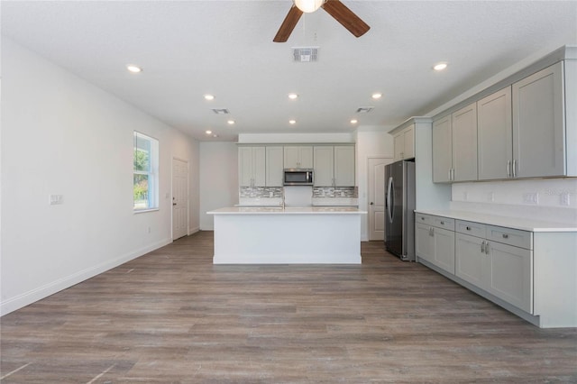 kitchen featuring light hardwood / wood-style flooring, a center island with sink, appliances with stainless steel finishes, gray cabinets, and backsplash