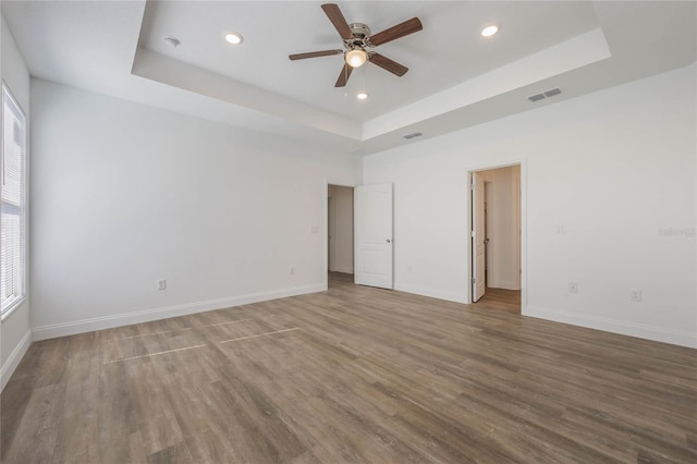 unfurnished room featuring a raised ceiling, wood-type flooring, plenty of natural light, and ceiling fan