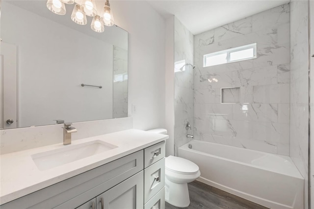 full bathroom with an inviting chandelier, hardwood / wood-style floors, vanity, tiled shower / bath, and toilet