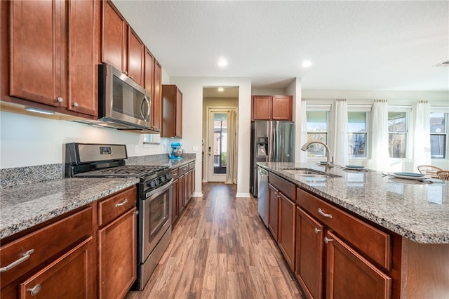 kitchen featuring a sink, light stone countertops, wood finished floors, stainless steel appliances, and a kitchen island with sink