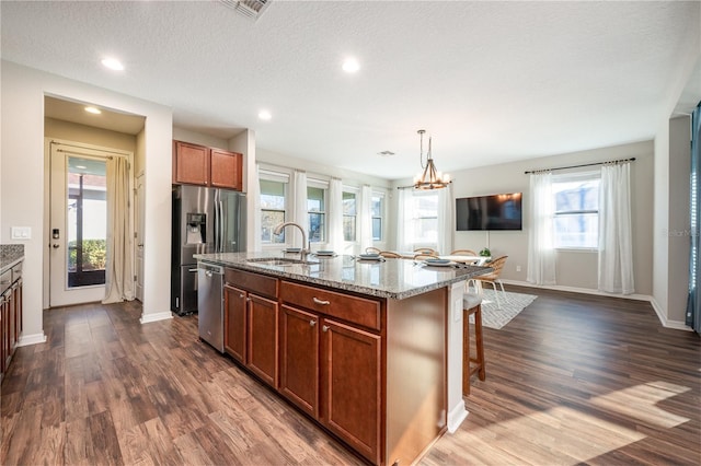 kitchen with appliances with stainless steel finishes, pendant lighting, sink, a kitchen island with sink, and light stone countertops