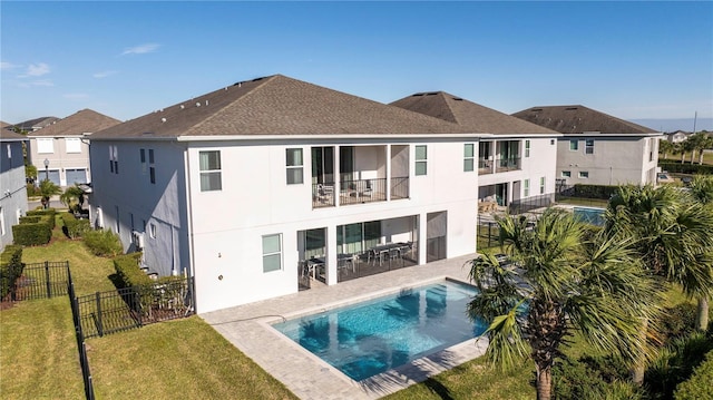 back of property featuring a fenced in pool, a patio, a balcony, and a lawn