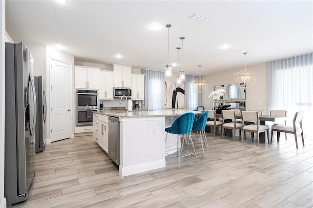 kitchen with white cabinetry, stainless steel appliances, decorative light fixtures, and a center island with sink