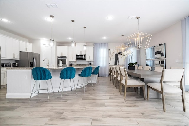 kitchen featuring hanging light fixtures, an island with sink, appliances with stainless steel finishes, and light stone counters