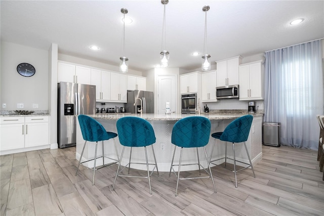 kitchen with pendant lighting, appliances with stainless steel finishes, light stone countertops, and an island with sink