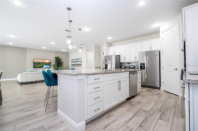 kitchen with white cabinetry, decorative light fixtures, stainless steel fridge, and an island with sink