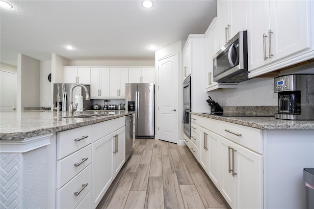 kitchen featuring sink, white cabinetry, light wood-type flooring, stainless steel appliances, and light stone countertops